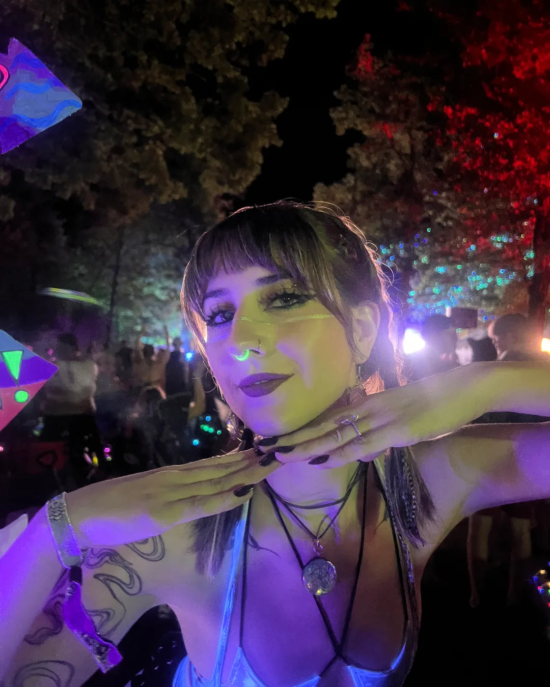 A festival-goer at night in a lit forest, the ring glowing under her nose